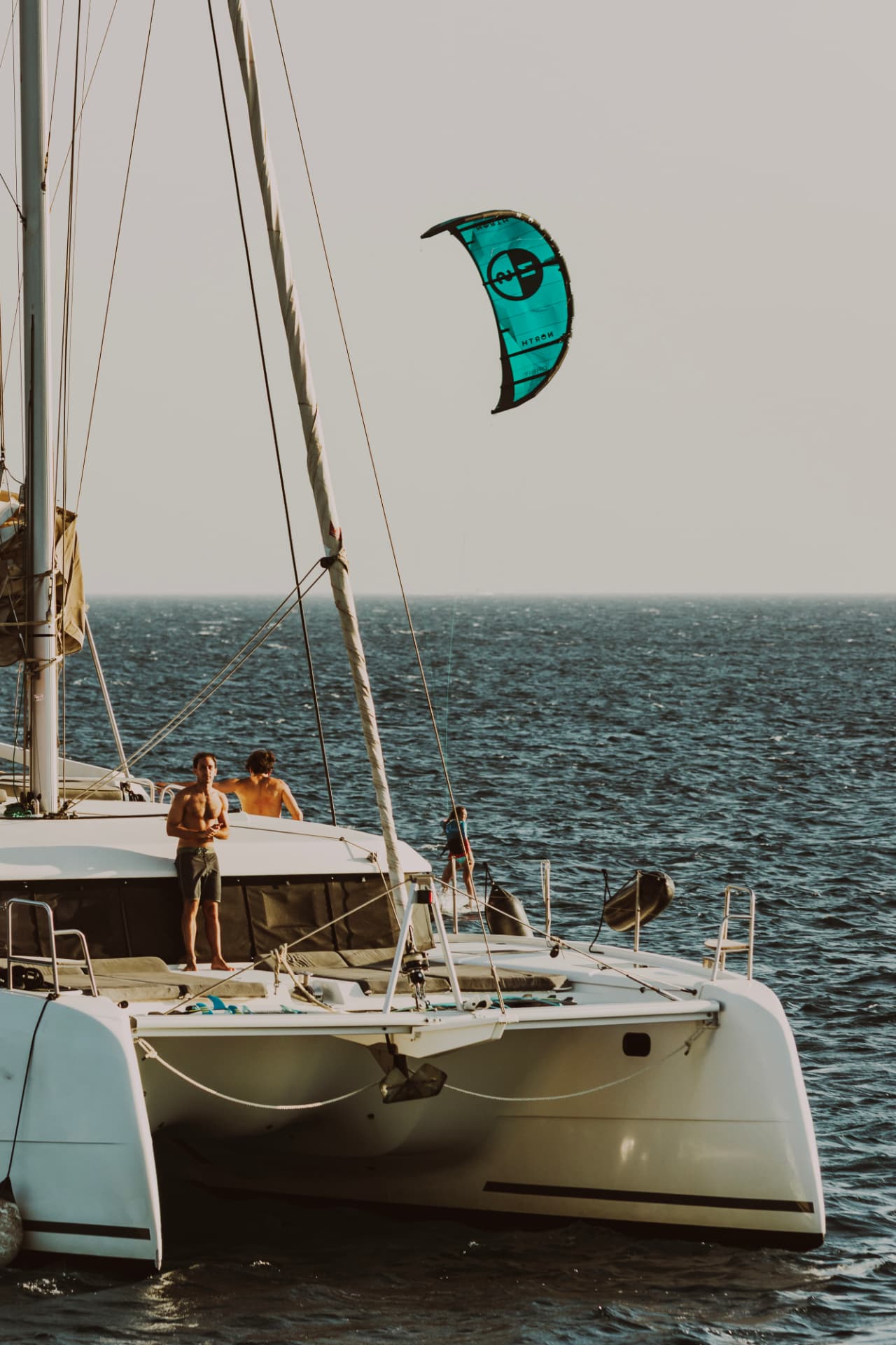 Catamaran at anchor with a teal kite in the air and two guests on deck