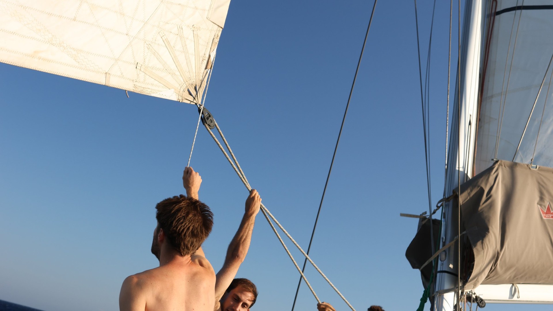 Crew member trimming the sail against a clear sky